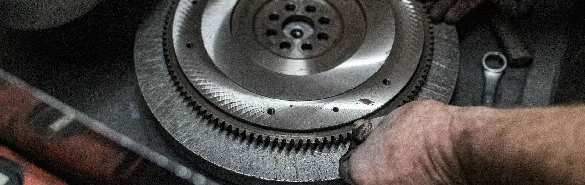 A hand holding a toothed metal flywheel in a workshop
